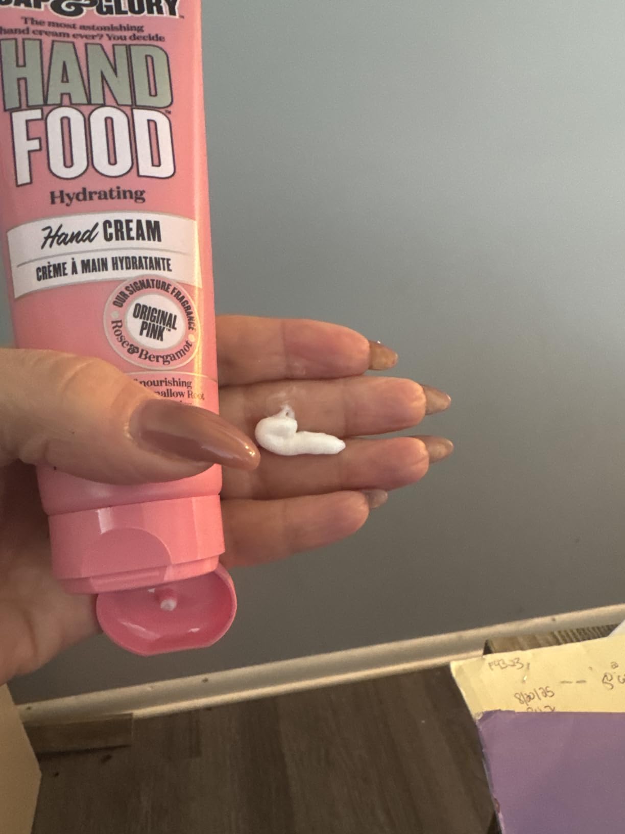 A hand holding a pink Soap & Glory Hand Food tube with a small blob of white hand cream squeezed onto the fingers