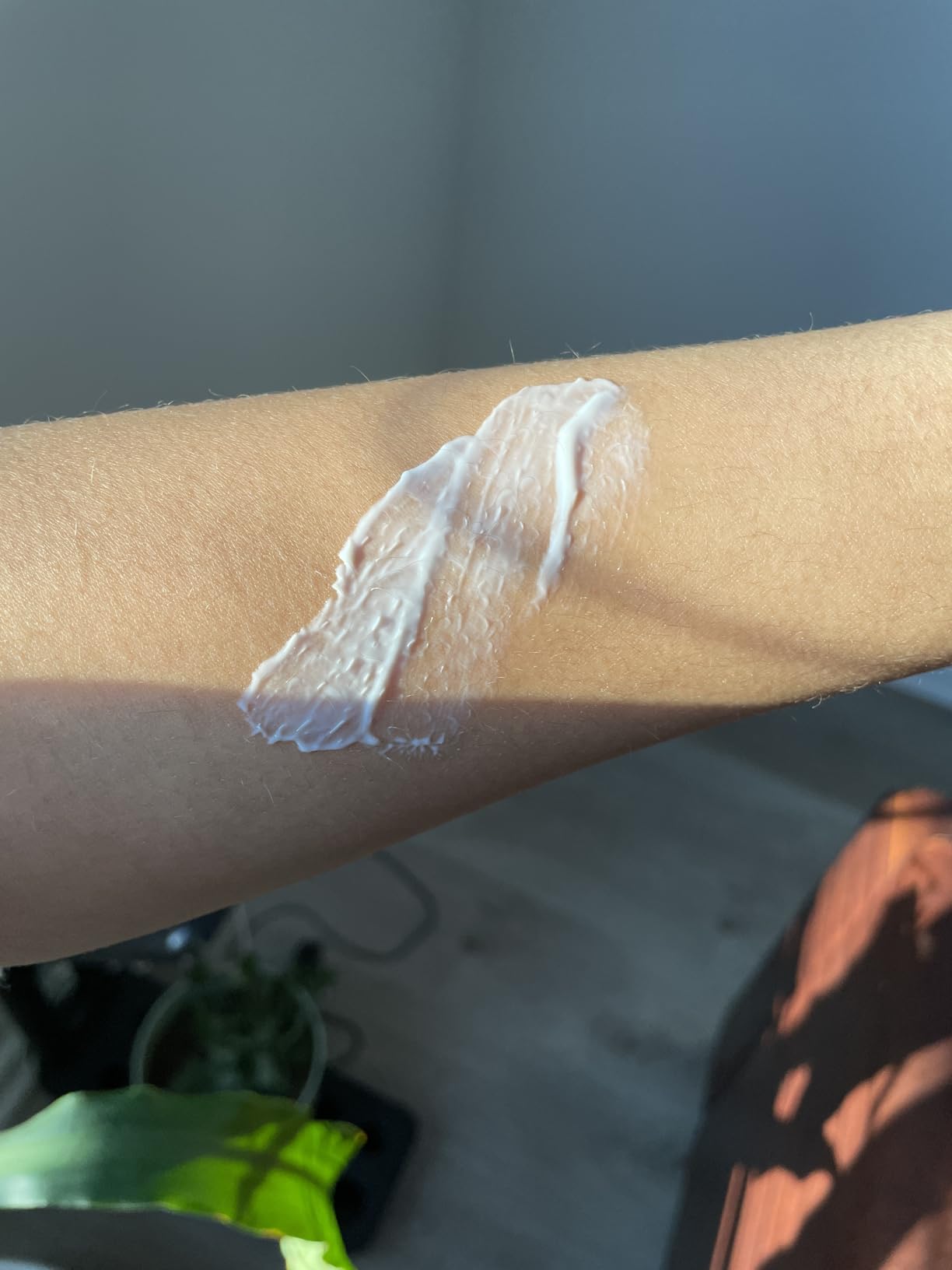 A thick stripe of pale pink body cream swatched across a forearm before it is rubbed in