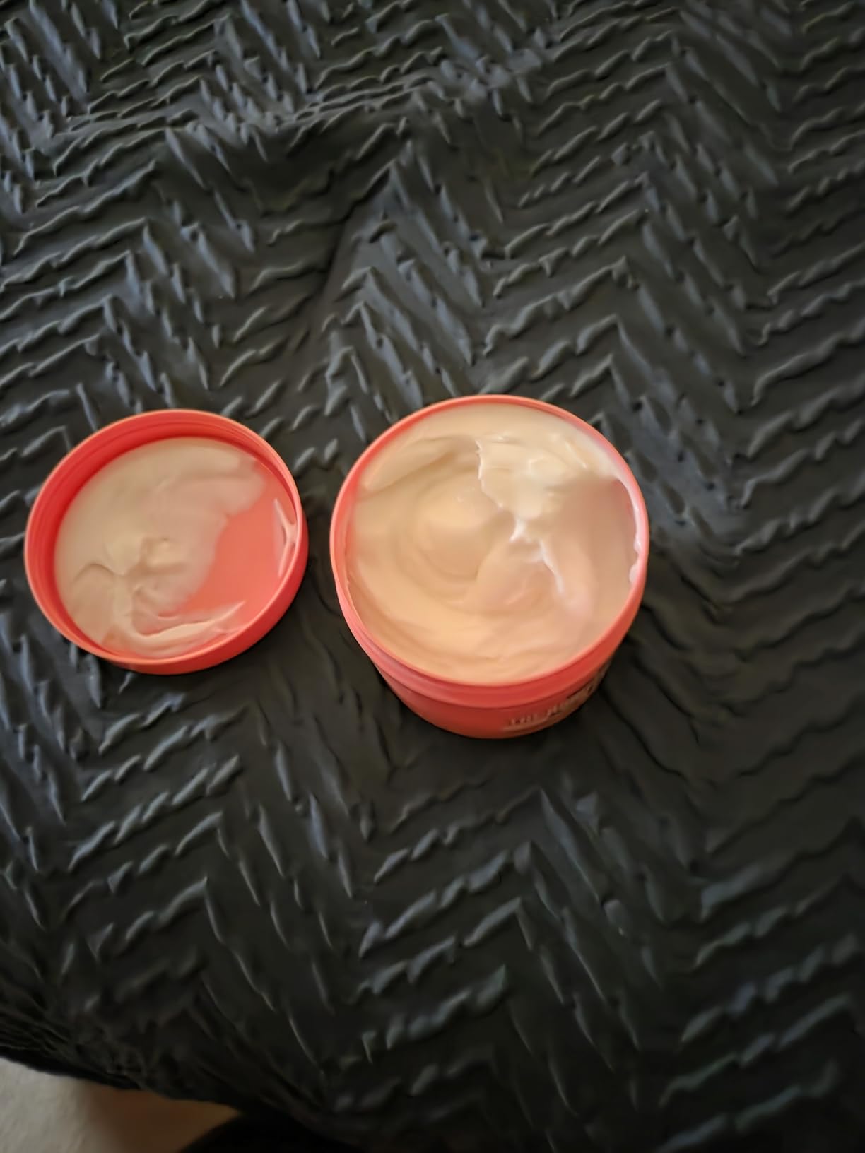 An open coral tub of Soap & Glory The Righteous Butter beside its lid, showing the whipped cream texture inside